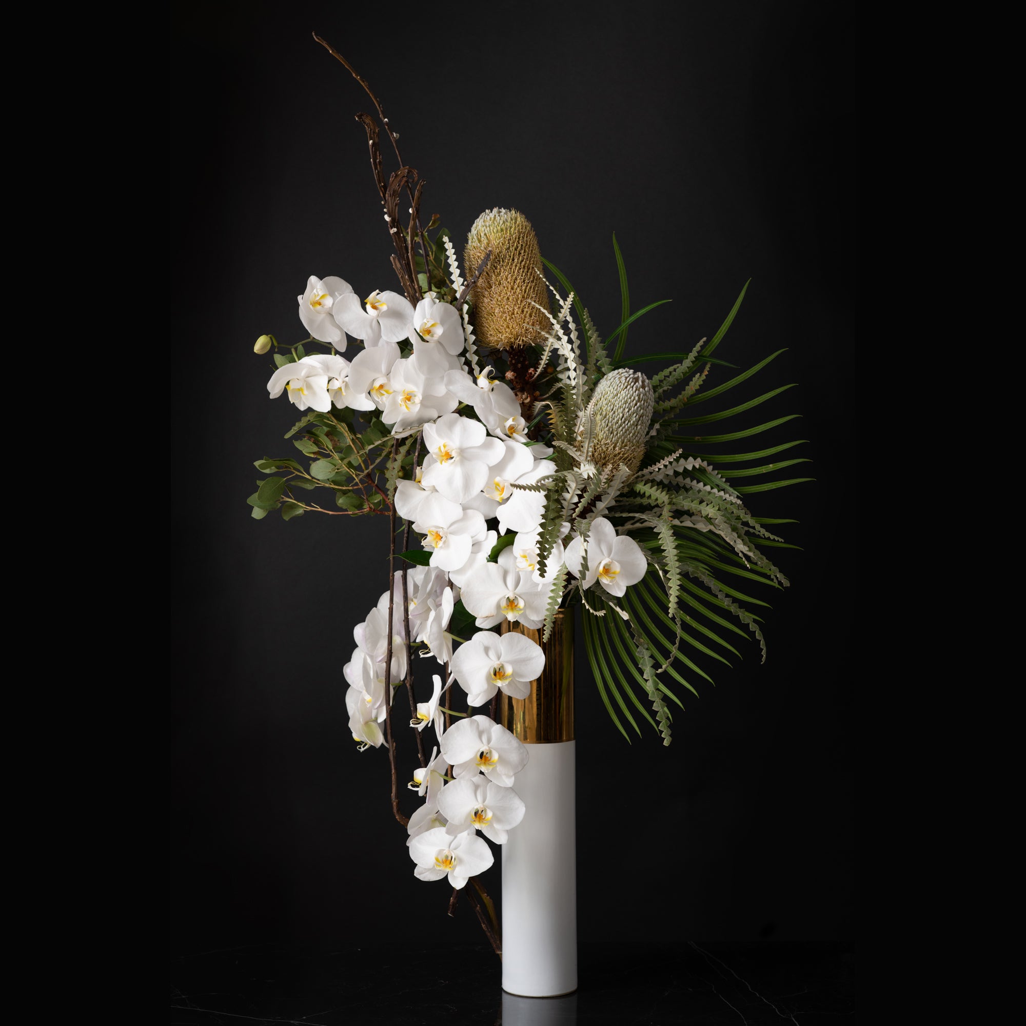 A stunning asymmetrical floral arrangement featuring cascading white orchids, sculptural banksia, and tropical greenery in a modern vase, designed by Bloom by Anuschka, alone of the best flower shops in Denver.
