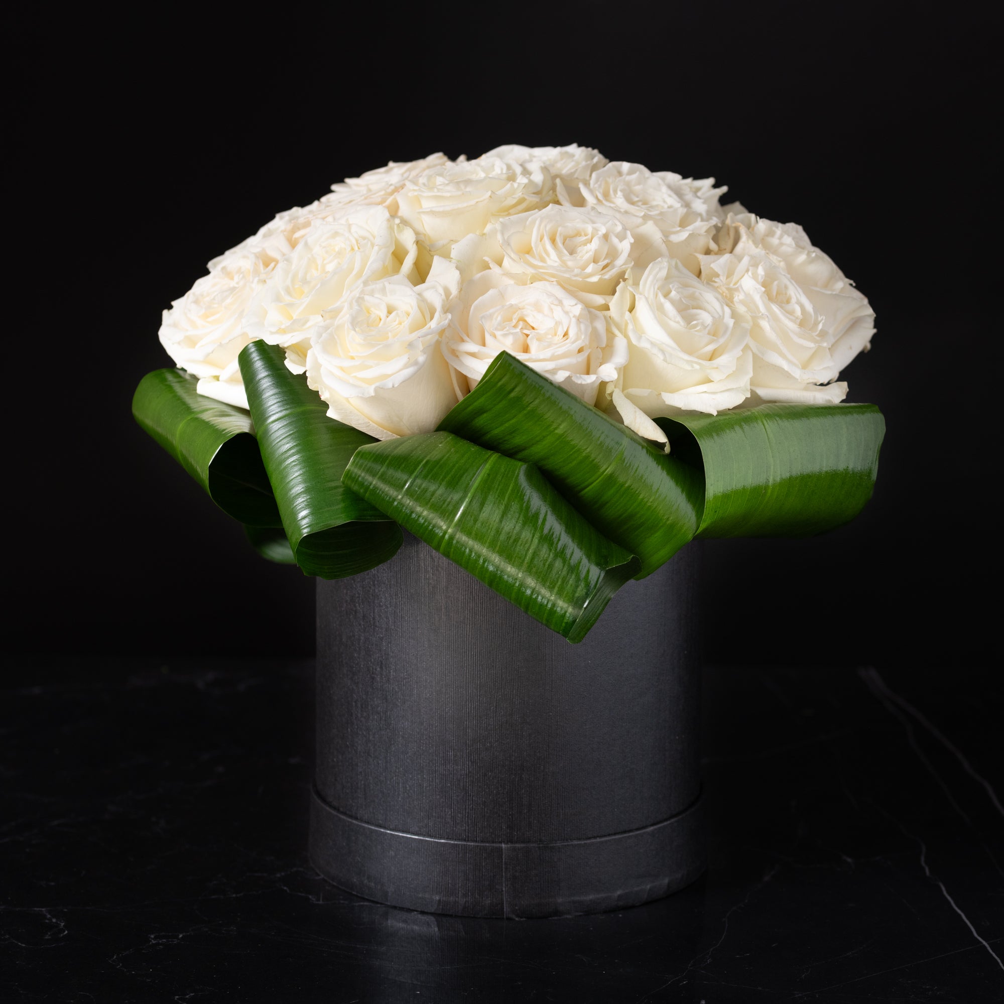 Pristine white roses arranged by Bloom by Anuschka in a charcoal hatbox, expertly crafted in our Denver flower shop