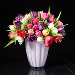A vibrant tulip arrangement in shades of red pink purple white and yellow artfully arranged in a white vase by Bloom by Anuschka a premier florist shop in Cherry Creek.