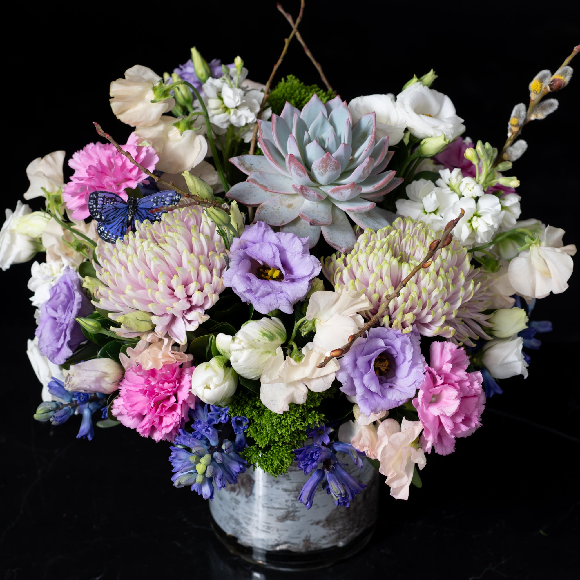 Elegant bouquet with pink, purple, and blue blooms, accented by succulents and seasonal greenery, showcasing Bloom by Anuschka’s fine flower crafting.