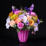 A bold and colorful floral arrangement featuring orchids roses gerbera daisies and carnations in a bright pink vase designed by Bloom by Anuschka a leading florist shop in Denver
