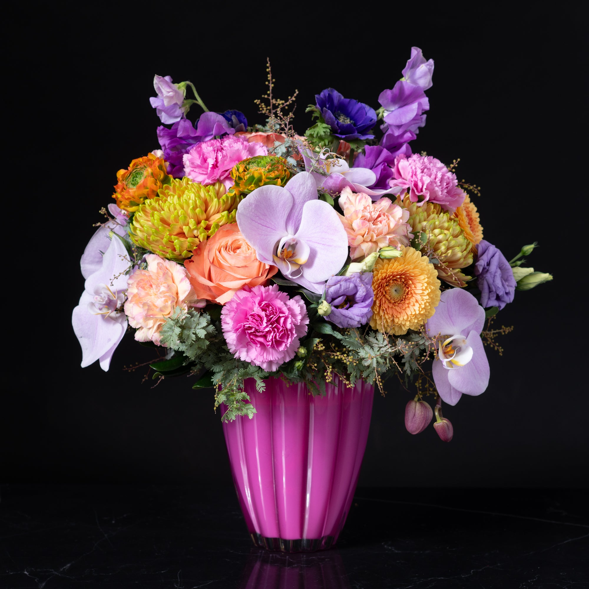 A bold and colorful floral arrangement featuring orchids roses gerbera daisies and carnations in a bright pink vase designed by Bloom by Anuschka a leading florist shop in Denver