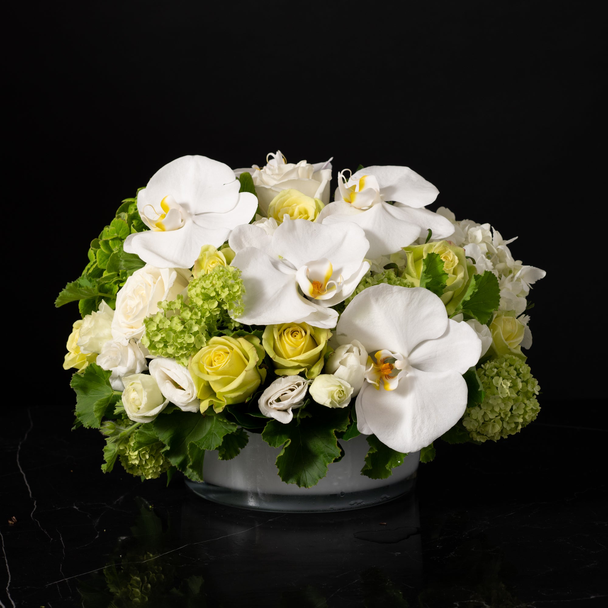 A luxurious white floral centerpiece featuring orchids, roses, and hydrangeas in a modern glass vase, designed by Bloom by Anuschka, a premier florist shop in Denver.