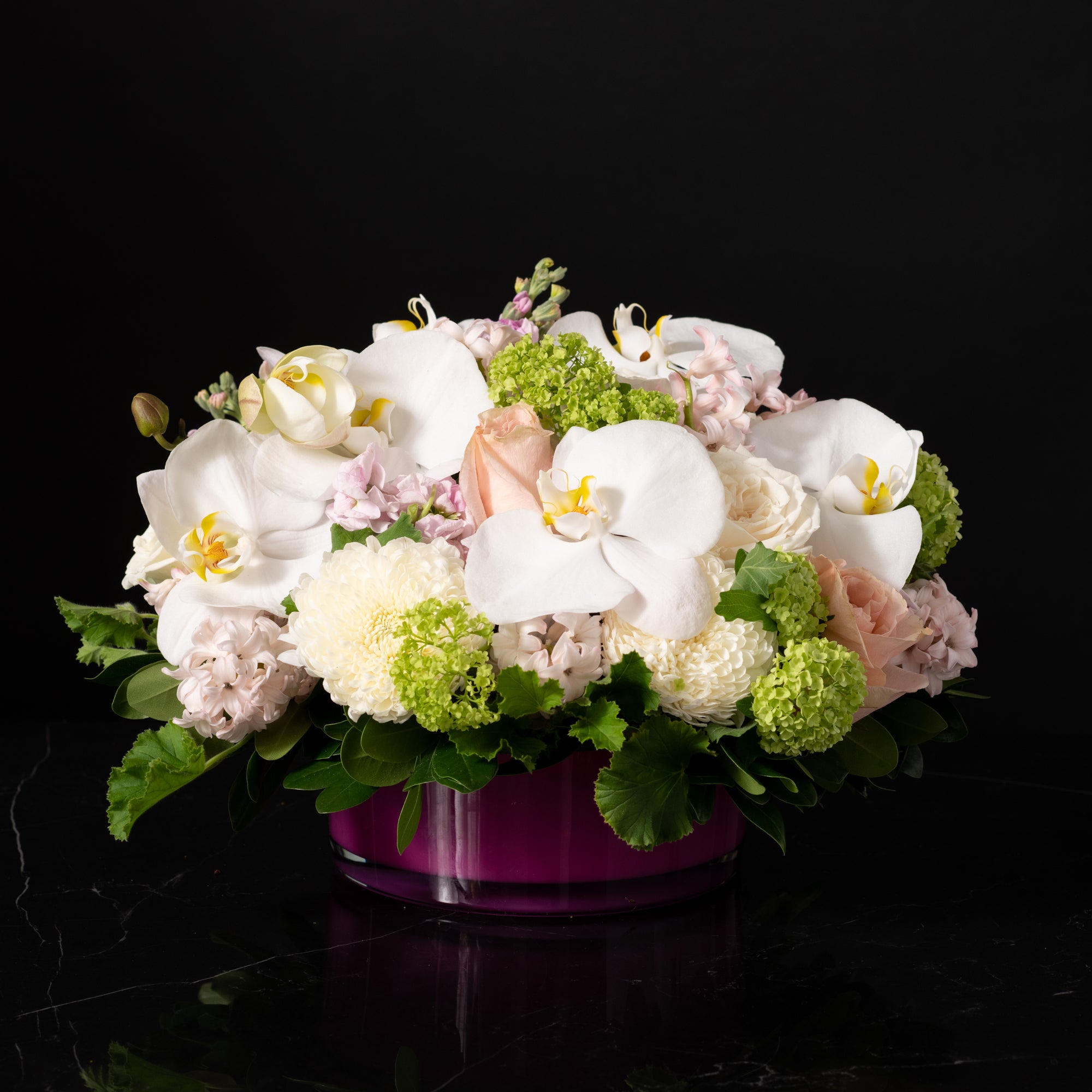 A luxurious floral centerpiece featuring cascading white orchids, blush roses, and hydrangeas in a deep purple vase, designed by Bloom by Anuschka, a premier florist shop in Denver.