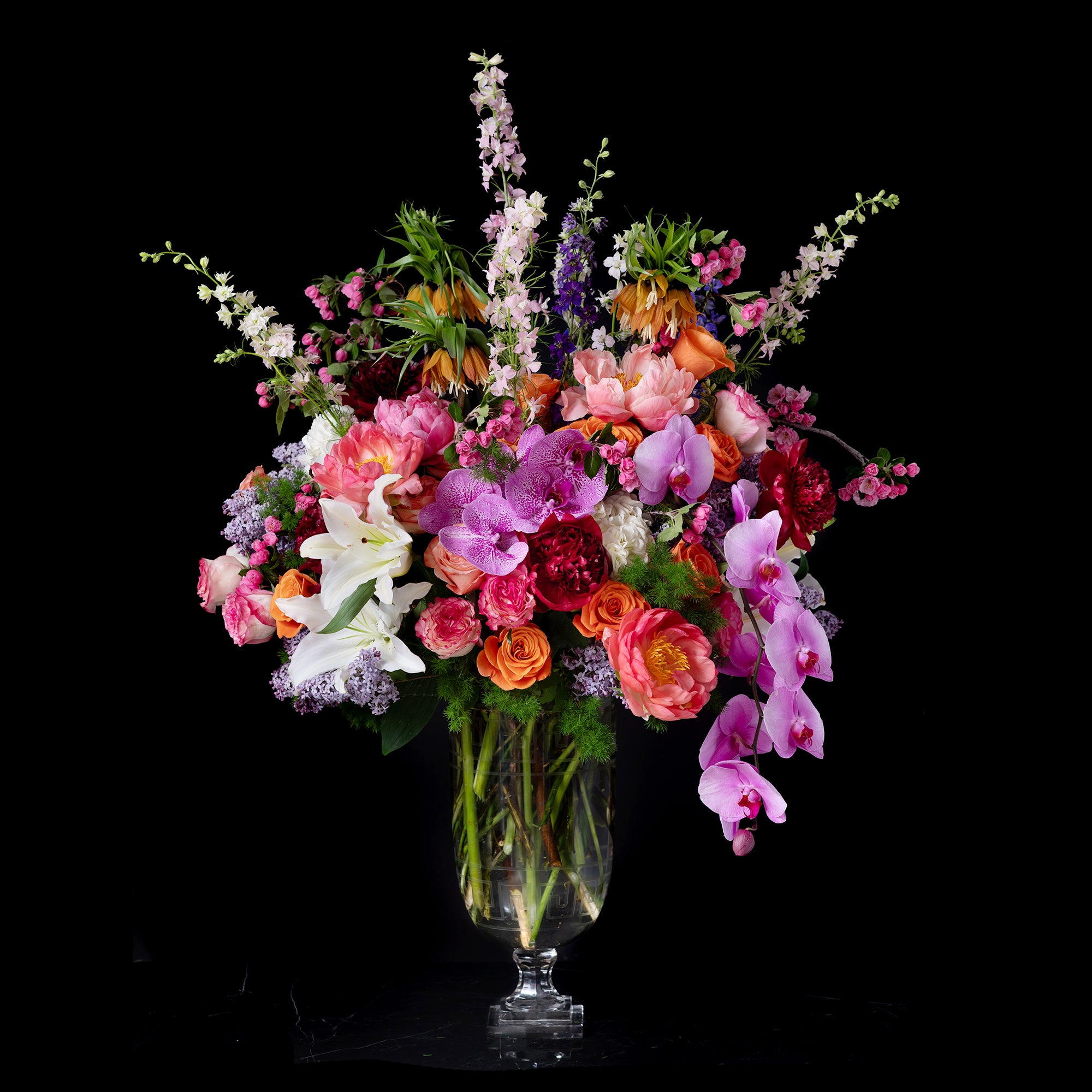A tall glass vase brimming with colorful orchids, peonies, roses, and lilies, embodying Bloom by Anuschka’s elevated florist shop craftsmanship.