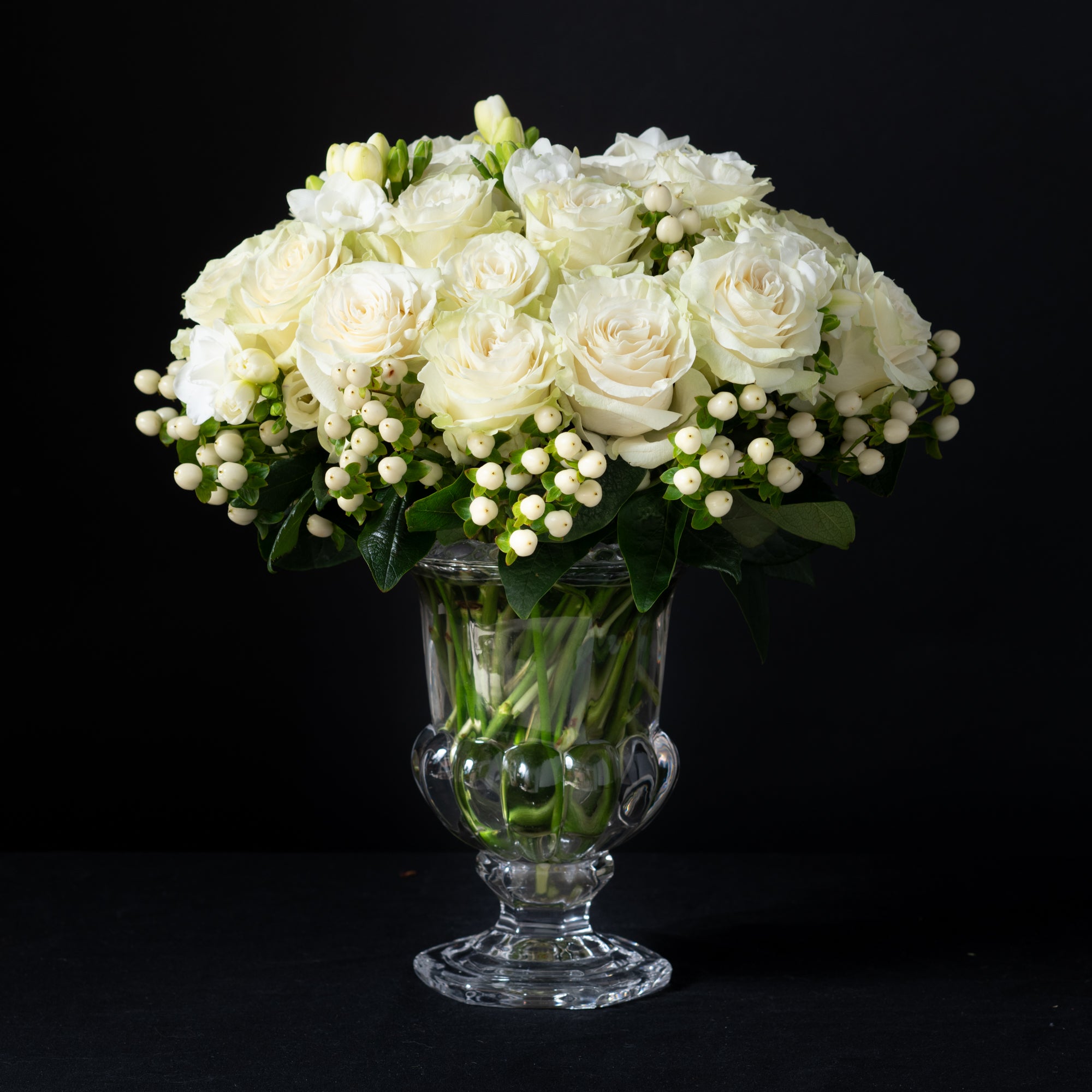 White roses, freesia, and hypericum berries arranged by Bloom by Anuschka in a pedestal vase, showcasing the artistry of florist’s design.