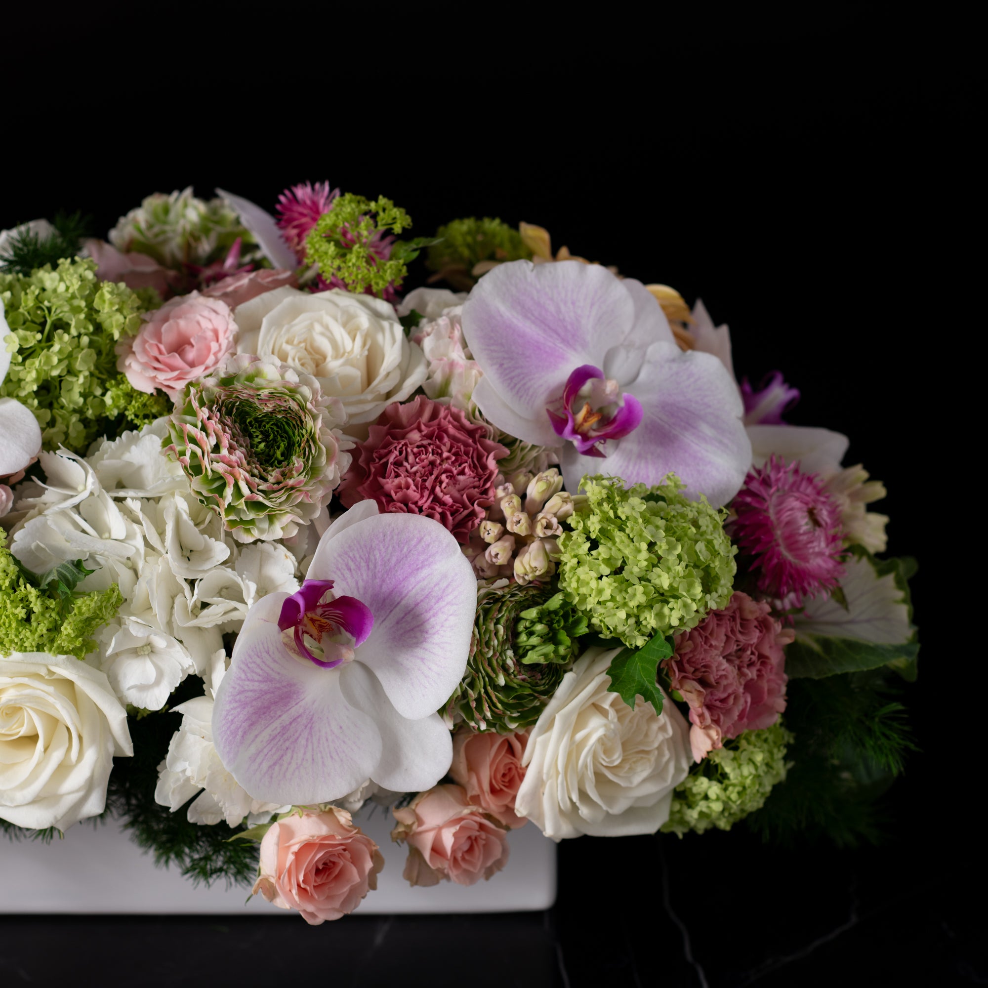 Close-up of delicate orchids, roses, and complementary flowers elegantly arranged by Bloom by Anuschka in a modern box, exemplifying a leading flower business.