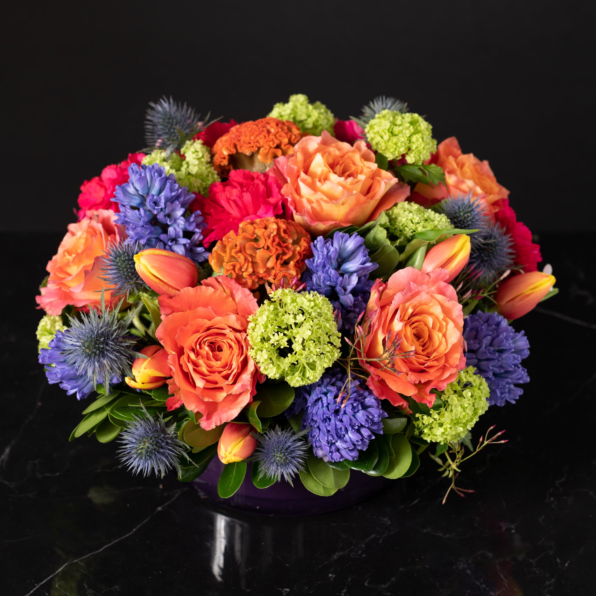Vibrant orange and blue floral centerpiece with tulips and lush greenery, showcasing Bloom by Anuschka’s signature flower crafting expertise.
